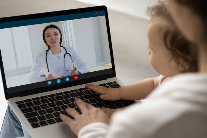 woman with a baby in her lap watching a webinar on her laptop